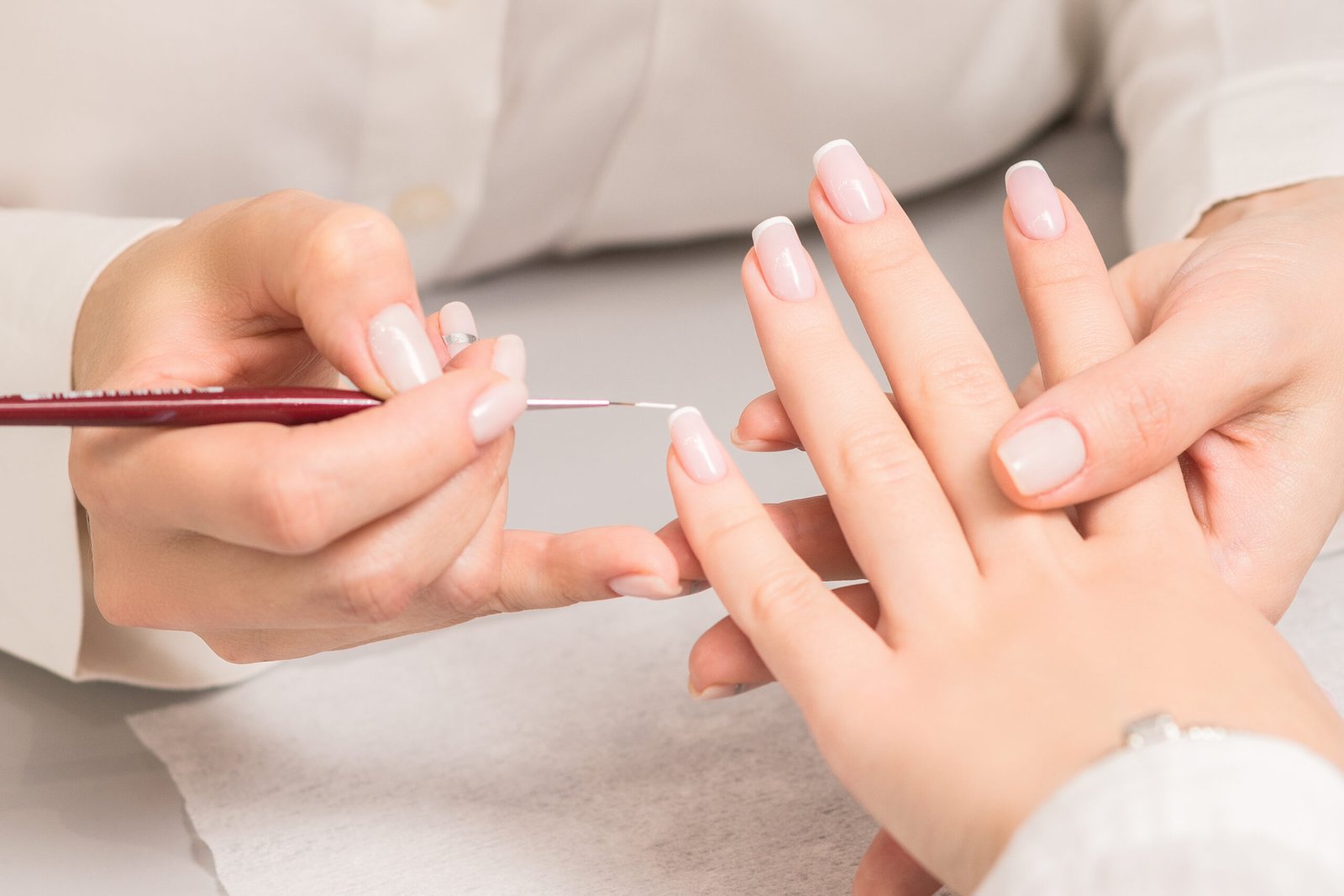 Hand of young woman receiving french manicure by beautician at nail salon.